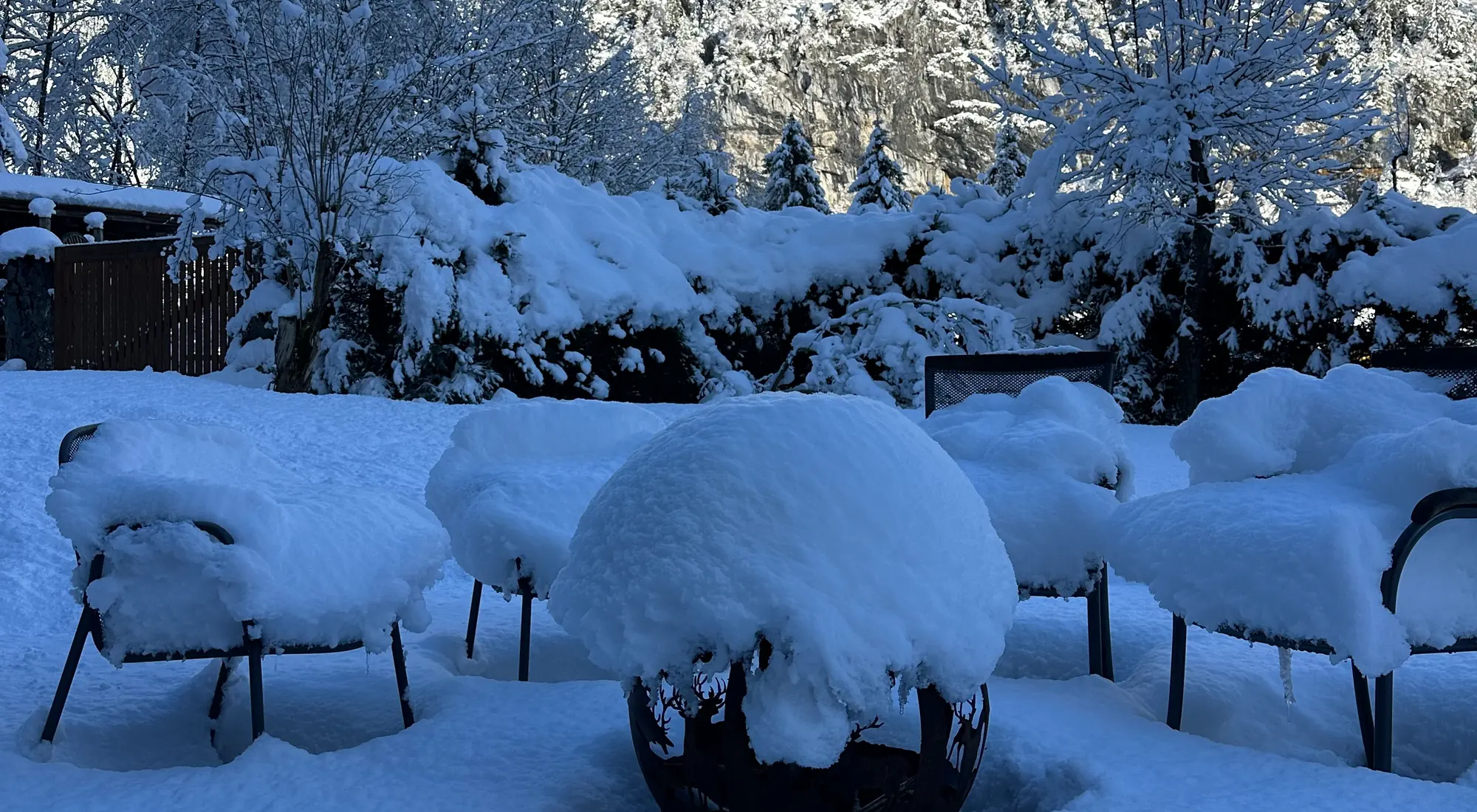 Fresh snowfall blanketing a chalet terrace and firepit below forested slopes in the Lauterbrunnen valley