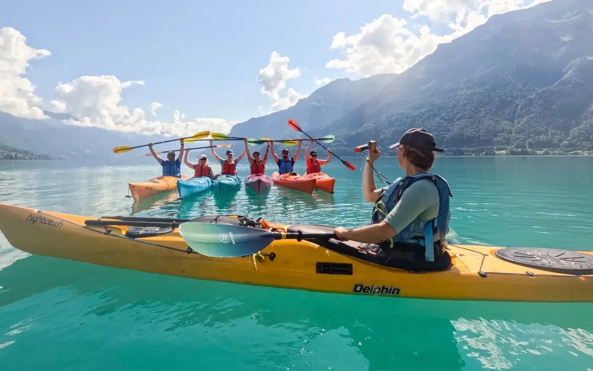 Grupo de kayakistas levantando los remos sobre el agua turquesa del lago de Brienz, con un guía en primer plano