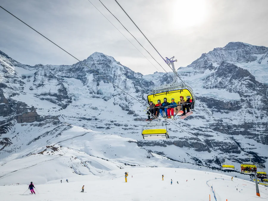 Skiers riding the yellow chairlift at Kleine Scheidegg with Mönch and Jungfrau behind