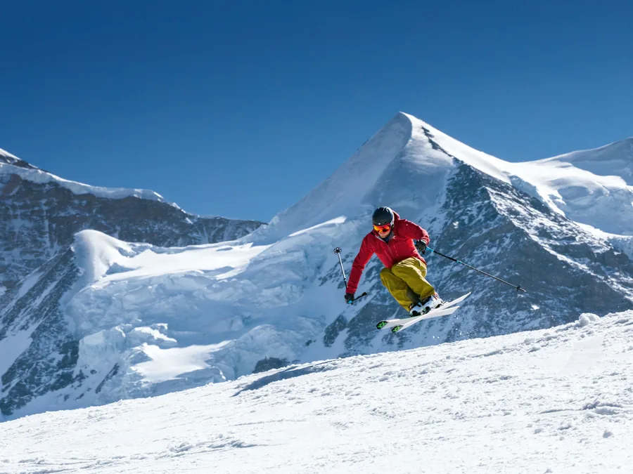 Skier catching air off a rise in the Mürren–Schilthorn ski area, snowy peaks behind