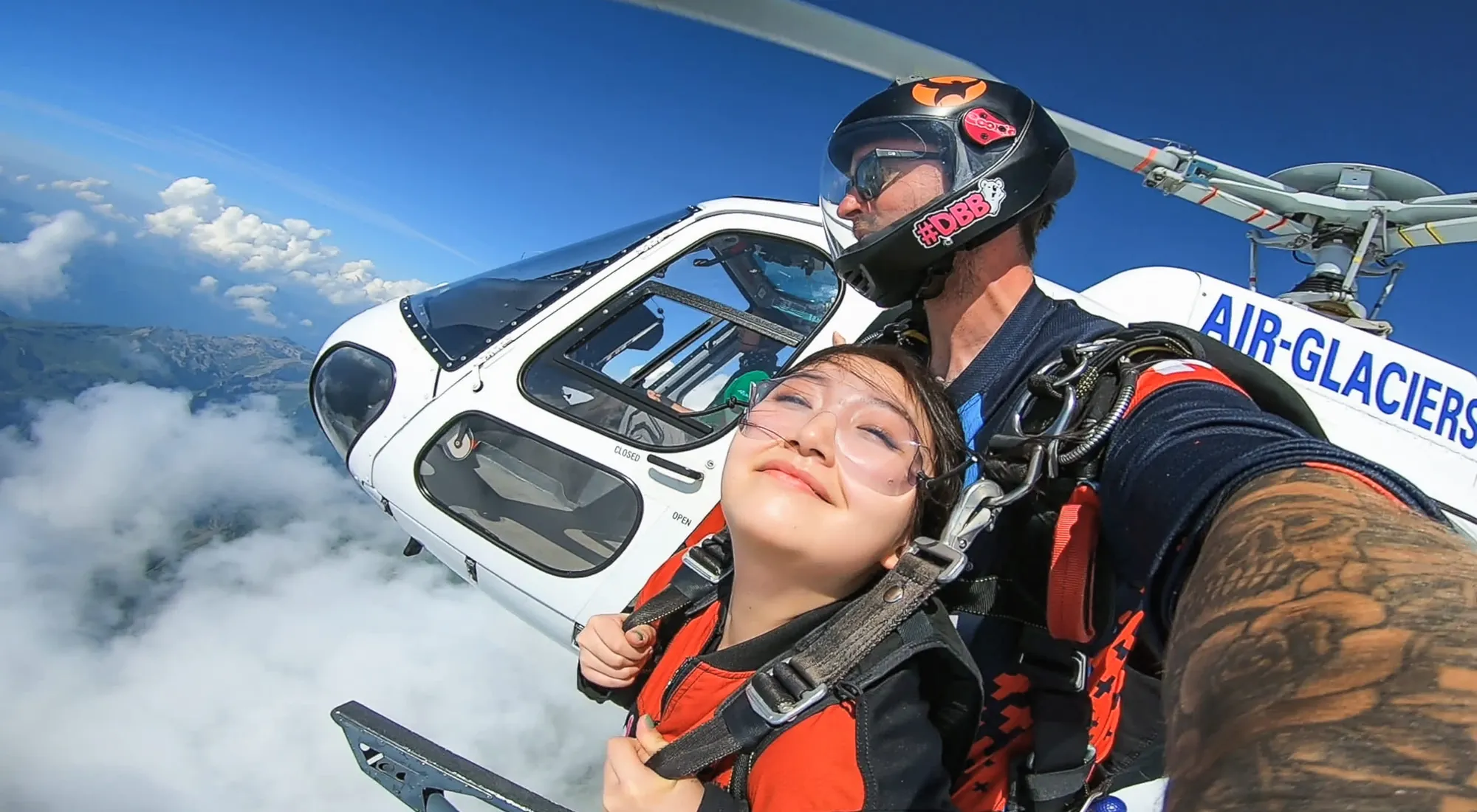 Tandemspringer neben einem Helikopter über den Wolken der Schweizer Alpen